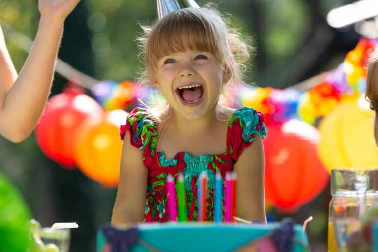 Smiling girl wearing colorful dress blowing out candles on birthday cake during party